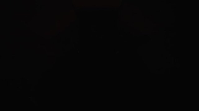A subtle fire dance behind a solid granite stone silhouette in 1000fps slow motion. Mirrored shadows and glowing edges create a mysterious noir atmosphere in a dark studio. Concept: shadow, silhouette