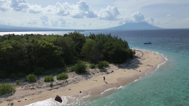 Tabuhan Island, East Java aerial zoom out of island and beach with volcano and boat visible in background