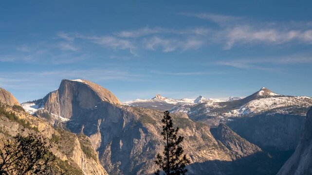 A majestic view of Yosemite Valley, featuring the iconic Half Dome and snow-capped mountains under a clear blue sky.