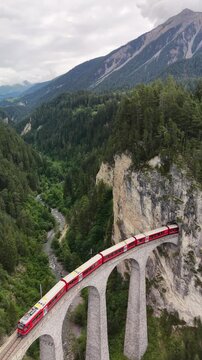 Portrait aerial drone footage of the iconic Landwasser Viaduct with a passing Rhaetian Railway train, captured from the air in the dramatic alpine landscape of Graub&uuml;nden, Switzerland &ndash; 2026
