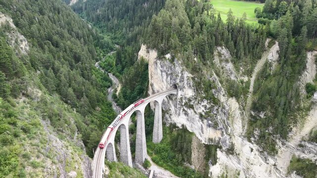 Cinematic aerial drone footage of the iconic Landwasser Viaduct with a passing Rhaetian Railway train, captured from the air in the dramatic alpine landscape of Graub&uuml;nden, Switzerland &ndash; 2026