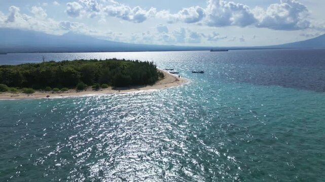Rapidly approaching a green, tropical island from the air, the sunny sky reflects on the tropical water. High to Low Angle Aerial View of Tabuhan Island, East Java