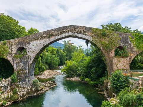 Ancient arched Roman bridge Cangas de Onis Spain. Historic stone bridge spans river in lush green surroundings in Picos de Europa