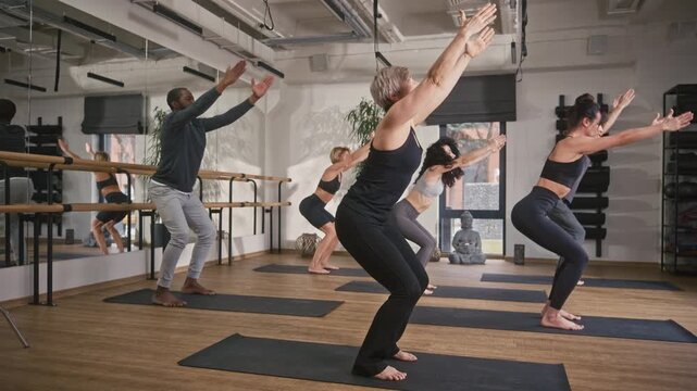 Multicultural people doing yoga asana at yoga studio. Group of yogi people standing at fitness mats. Yoga coach conducting spiritual yoga class. Multiethnic people doing meditation pose at yoga class.