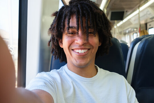 A young man smiles and takes a selfie while riding the train