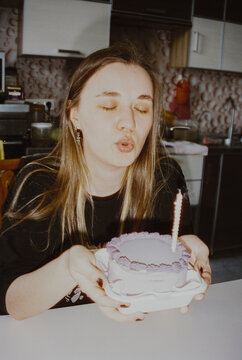 A young woman blows out a candle on a birthday cake at home