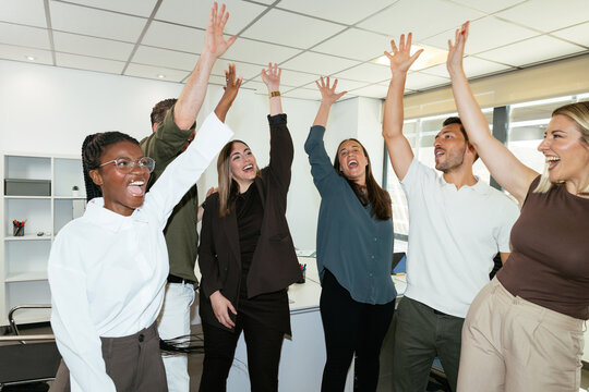 Diverse business team celebrating success raising arms in office