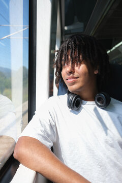 Young Man Enjoys Train Ride While Looking out Window on Sunny Day