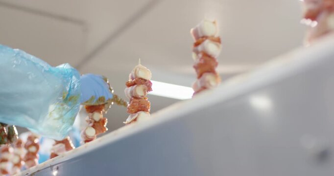 Gloved hand marinating bacon wrapped meat skewers in a food plant