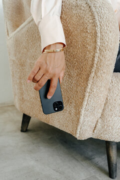 Close-Up of Businesswoman Holding Smartphone Beside Textured Armchair