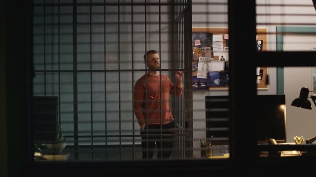 Bored male inmate standing behind jail cell bars, waiting for release