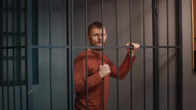 Young man standing behind jail cell bars after arrest for a minor offense