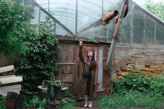 Woman holding large leaf as umbrella in garden near greenhouse