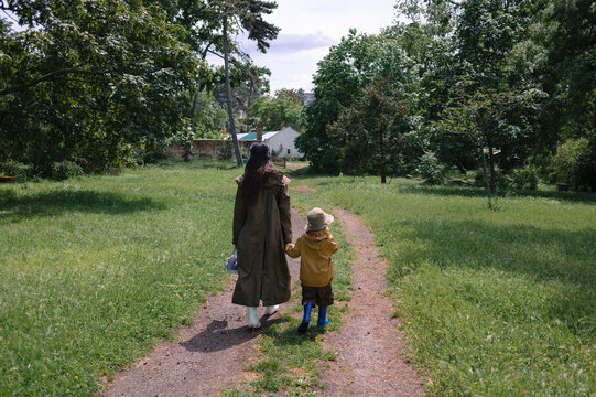 Mother and child walking hand in hand in a park wearing raincoats