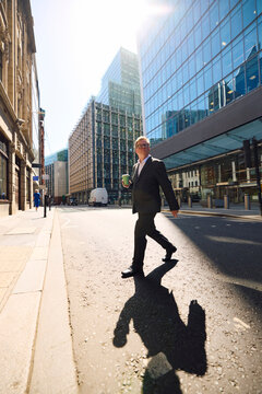 Businessman crosses the street with a cup of coffee in hand.