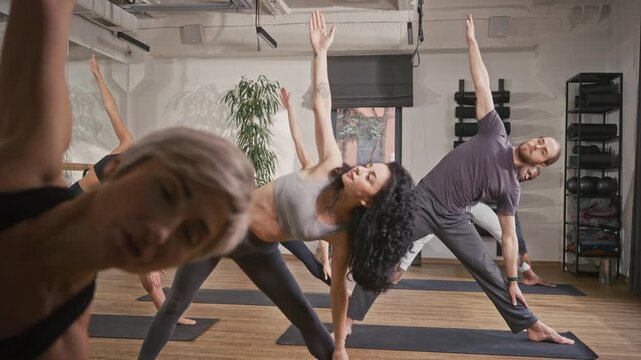 Group of people practicing vinyasa yoga pose. Man and women doing meditation pose at yoga studio. Mindfull people bending at side at yoga session. People relaxing and catching spiritual zen.