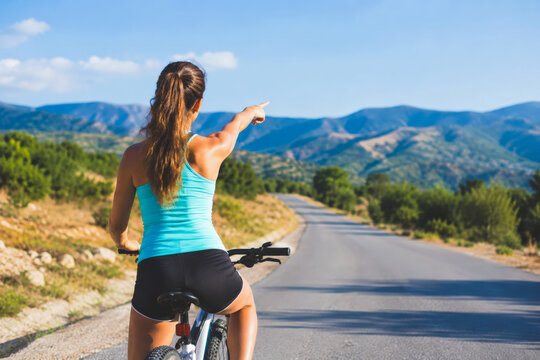 Woman cycling on a countryside road in summer, pointing into the distance