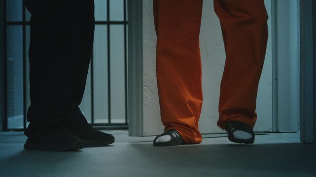 Prison guard escorting a male inmate in an orange prison uniform out of cell