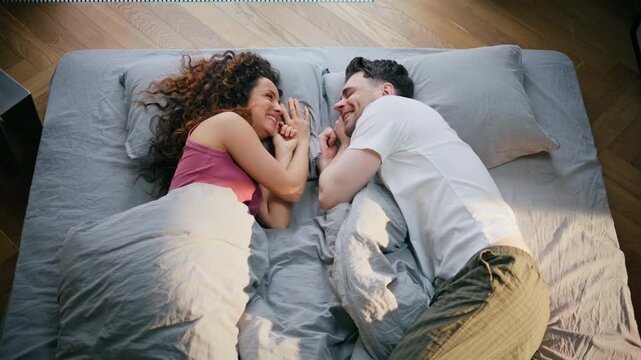 Overhead couple lying bed touching hands. Loving pair face to face bedroom