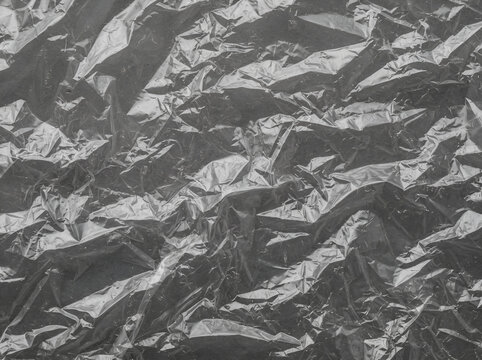 Textured black crumpled plastic sheet with detailed wrinkles and high contrast reflections for abstract background