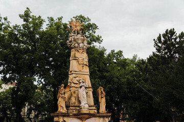 Fototapeta premium Historic stone monument surrounded by mature trees in a peaceful urban park. Sculptural composition reflecting the cultural heritage of Subotica, Serbia.