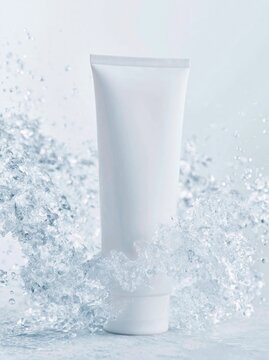 Unlabelled white skincare tube standing upright surrounded by splashes of water against a soft blue background, highlighting product design and texture