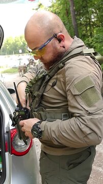 A tactical officer stands beside an open vehicle,carefully adjusting protective gear and communication equipment before a field mission.Professional military preparation in an outdoor woodland setting