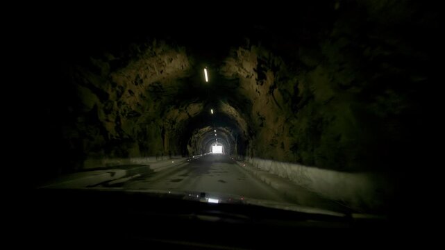 A car drives through a mountain tunnel in the Austrian Alps (Tyrol). A view from inside the car, through the windshield, of the illuminated mountain tunnel.