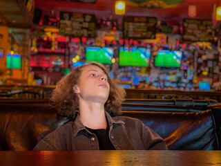 Teen Relaxing in Sports Bar with Screens in Background, for Youth Leisure, Watching Live Sports, Entertainment Venues, Social Recreation, and Weekend Activities © KRISTINA KUPTSEVICH