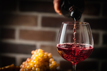 Obraz premium Pouring red wine into the glass on rustic dark background. Pour alcohol, winery concept.