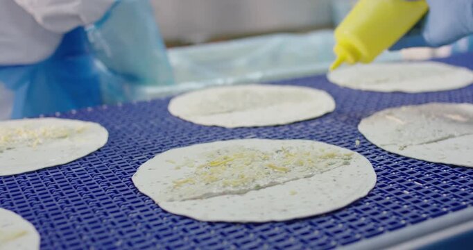 Hands top round flatbreads with cheese on a blue conveyor
