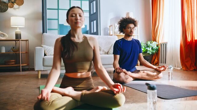 Multiracial couple meditating in lotus pose at home. Yoga mindfulness practice