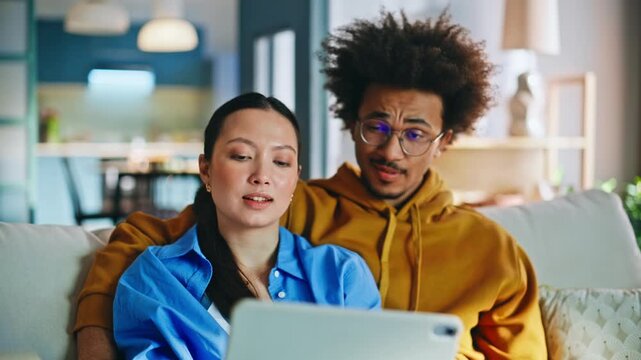 Multiethnic couple browsing tablet sofa. Pair shopping online together at home.
