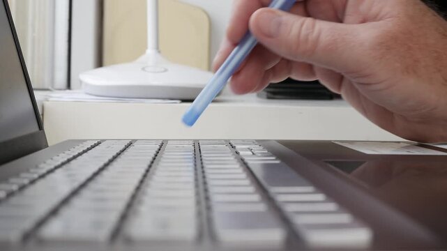 Hand Holding Blue Pen Writing on Laptop Keyboard. Typing on Laptop Keyboard Closeup Detail.