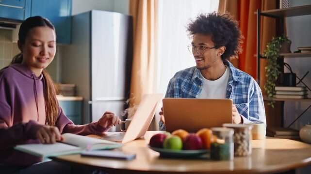 Young multiethnic couple studying together with laptops in cozy home kitchen