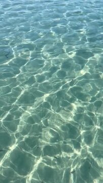 Transparent turquoise sea water ripples reflection on sand sunlight glare.Sea floor pattern background.