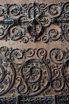 Vertical close-up of decorative wrought iron ornamentation on the historic wooden doors of Notre-Dame Cathedral in Paris, France, highlighting Gothic floral scrollwork, symmetry