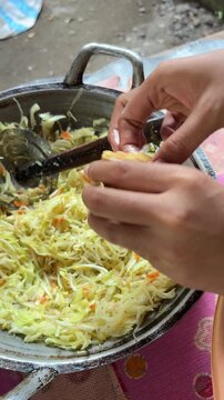 Close-up of hands stuffing fried tofu with shredded vegetables for traditional Tahu Isi preparation.