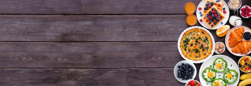 Breakfast or brunch side border on a dark wood banner background. Top down view. Assortment of fruits and sweet and savory food items. Copy space.