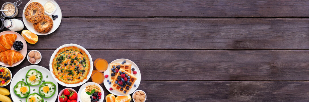 Breakfast or brunch corner border on a dark wood banner background. Above view. Assorted fruits and sweet and savory food items. Copy space.