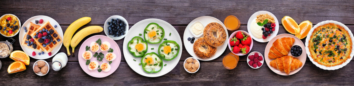 Breakfast or brunch table scene on a dark wood banner background. Top down view. Variety of fruits and sweet and savory food items.