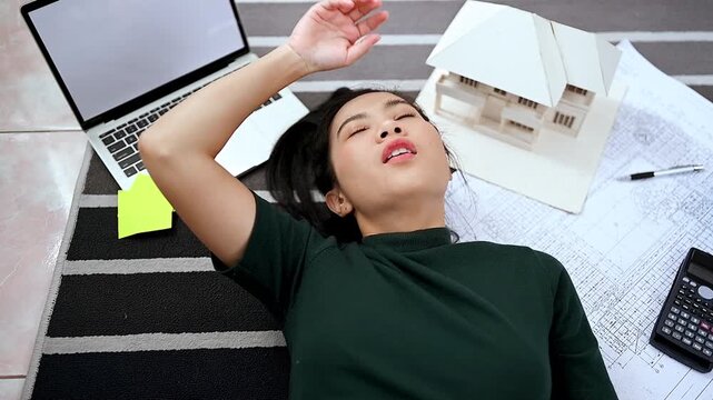 Burned-out architect lying among plans, laptop and house model