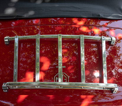 TAVERNES BLANQUES, SPAIN - JUNE 14, 2026.Close up view of chrome luggage rack on red trunk lid of vintage MG MGB roadster with tree reflections