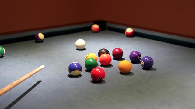 Pool cue hitting cue ball to strike numbered nine ball on billiard table close up.
