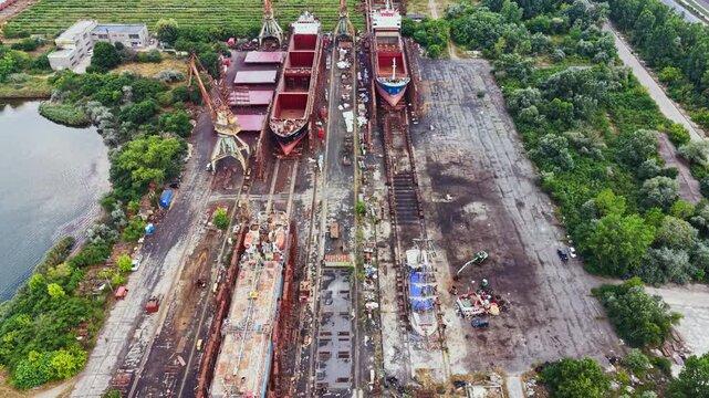 Workers construct and repair ships in a large shipyard filled with several vessels. Equipment and materials are scattered around as activities take place.