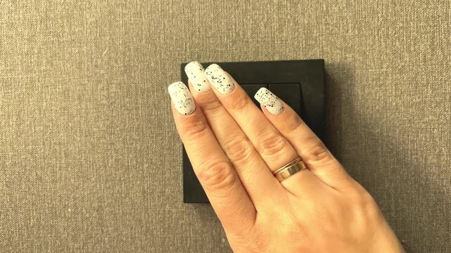 A hand flips a black light switch on a wall, home electricity control, everyday household routine, modern interior, residential lifestyle.