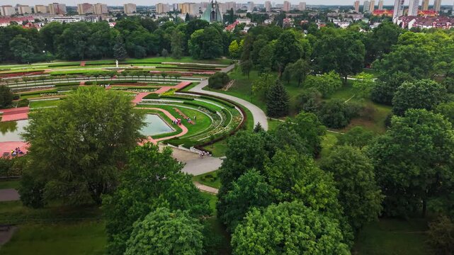 aerial perspective capturing a meticulously landscaped public park with a large pond, extensive terraced flower beds drone view