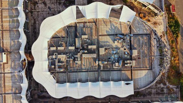 Workers are busy at a construction site as they install building materials on the roof of a large structure. Machinery and tools are scattered around.