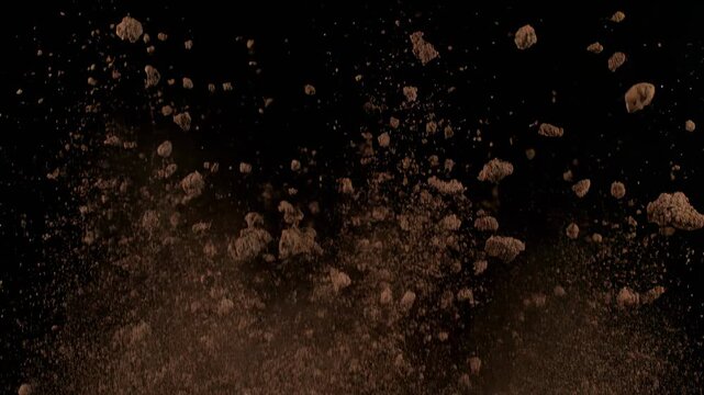 Ground breaking dirt explosion with rocky debris during daylight cinematic motion against black background