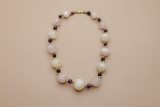 Elegant Necklace with Round Pastel Beads and Small Dark Accents, Displayed Artfully on a Soft Beige Background, Ideal for Jewelry Showcases